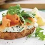 wholegrain bread with herb cottage cheese smoked salmon and arugula on white plate
