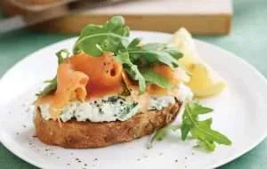 wholegrain bread with herb cottage cheese smoked salmon and arugula on white plate